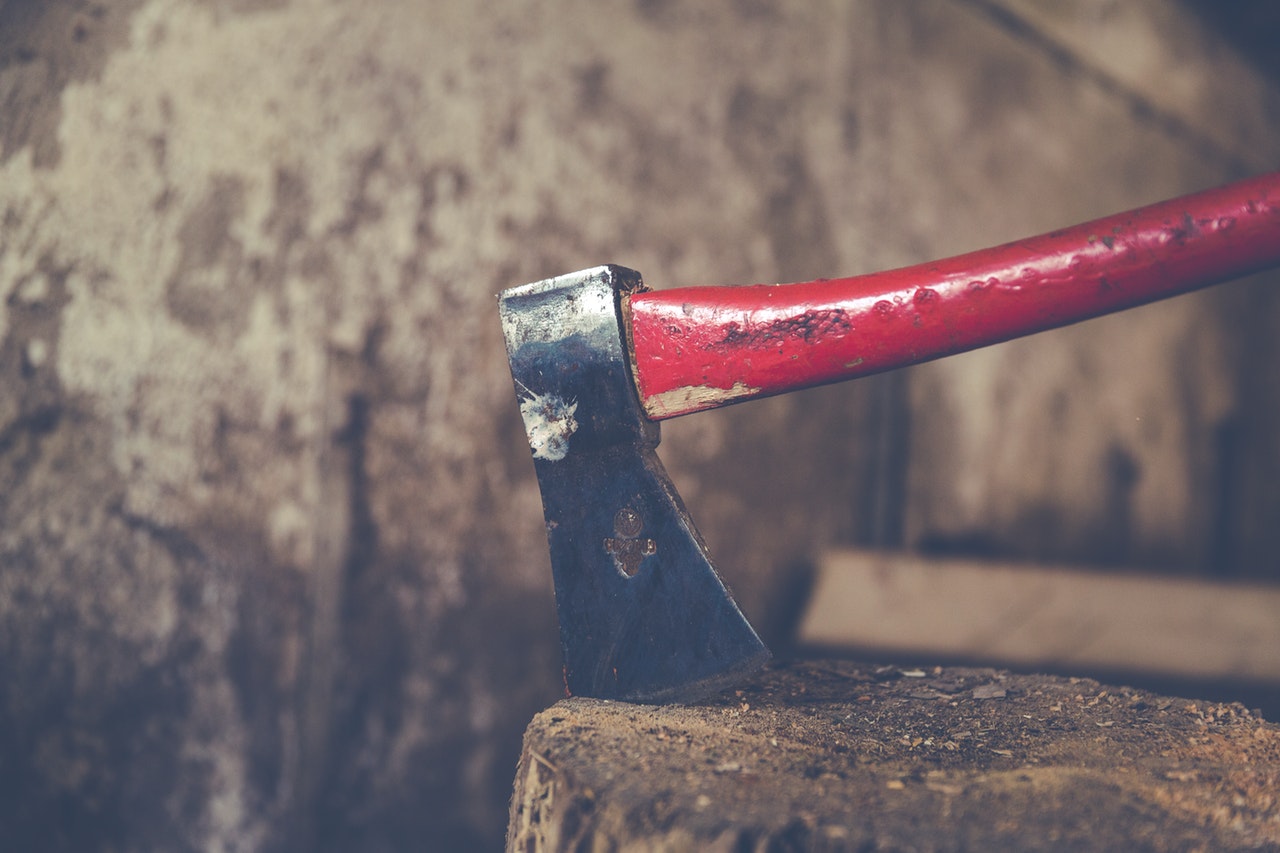 Red-handled axe buried in a tree stump.