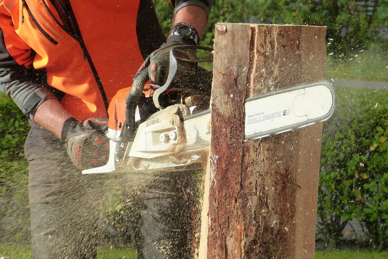 Man in orange safety vest chainsawing a tree trunk vertically