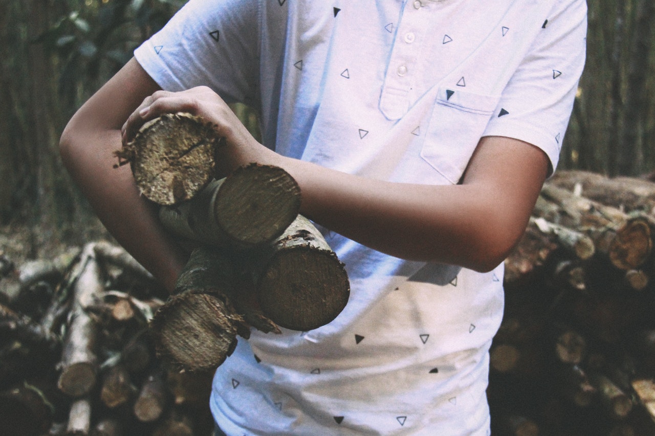 Man in patterned white shirt holding four logs under his right arm